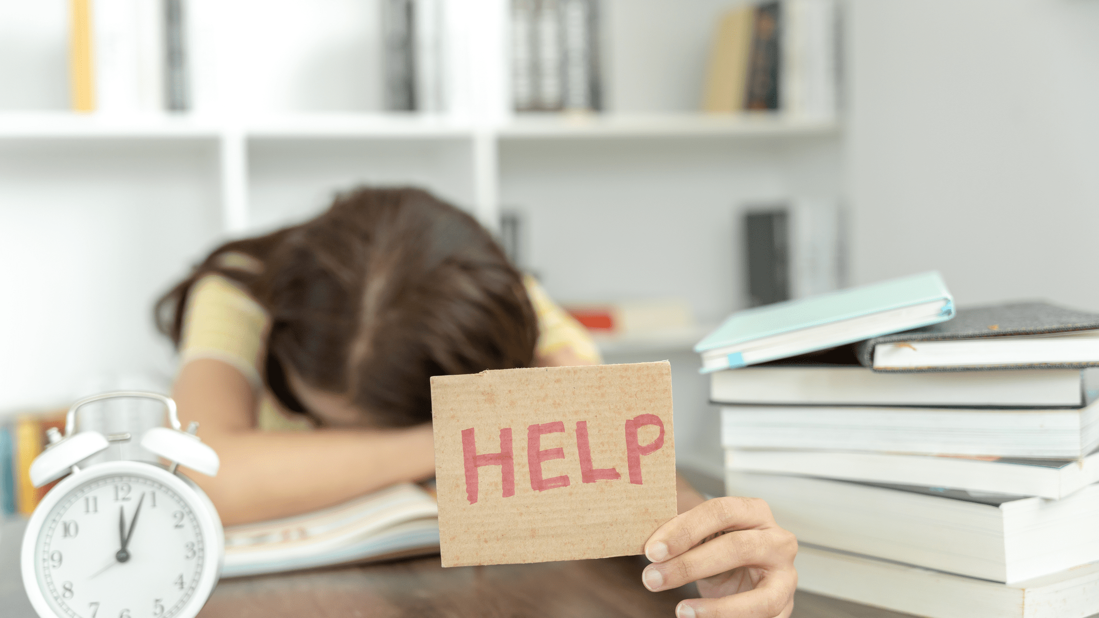 A medical school student laying her head down on a pile of USMLE Step 1 study books, holding up a "help" sign.