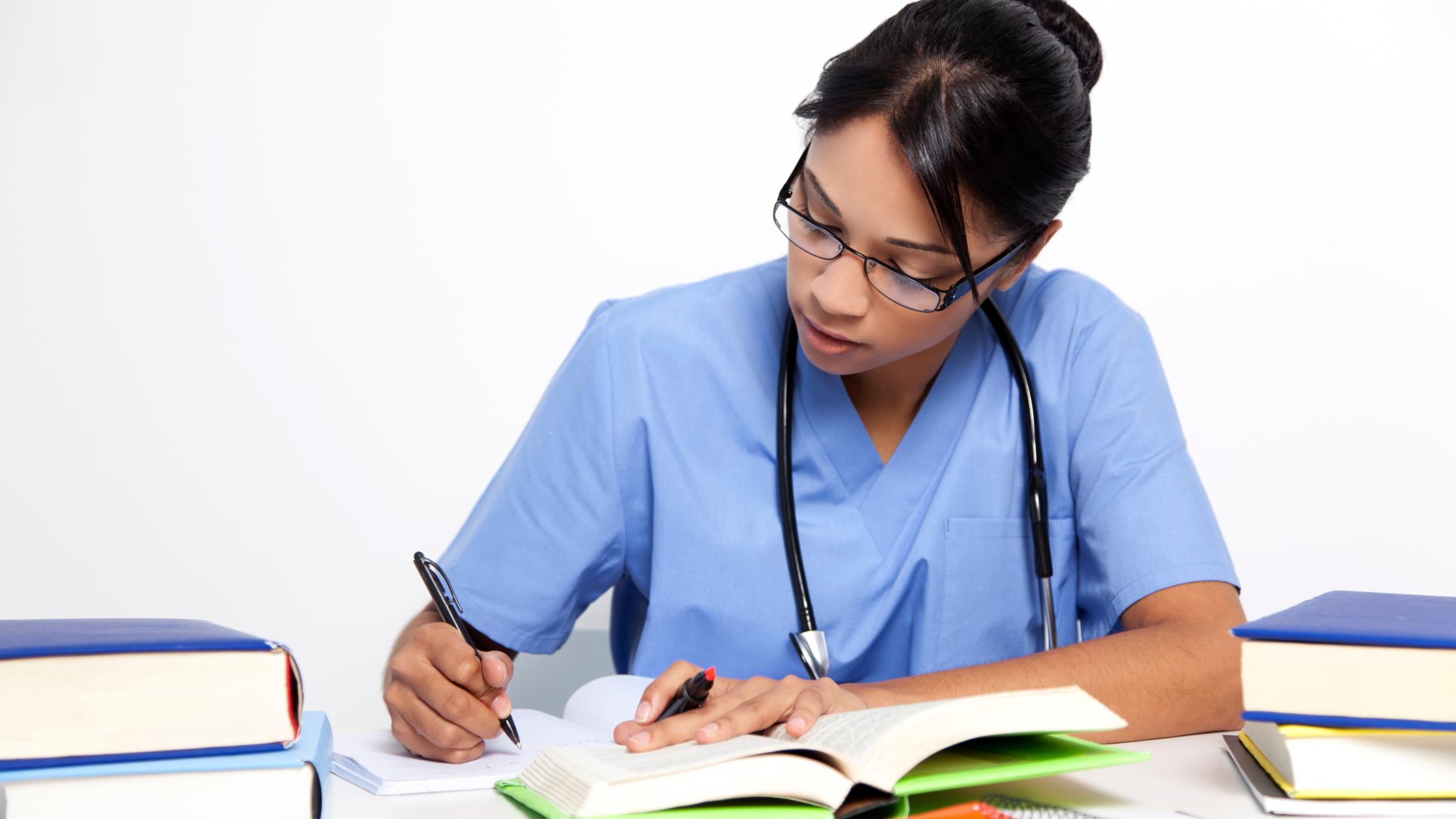 A medical resident wearing scrubs, studying for the USMLE Step 3 CCS in front of notebooks.