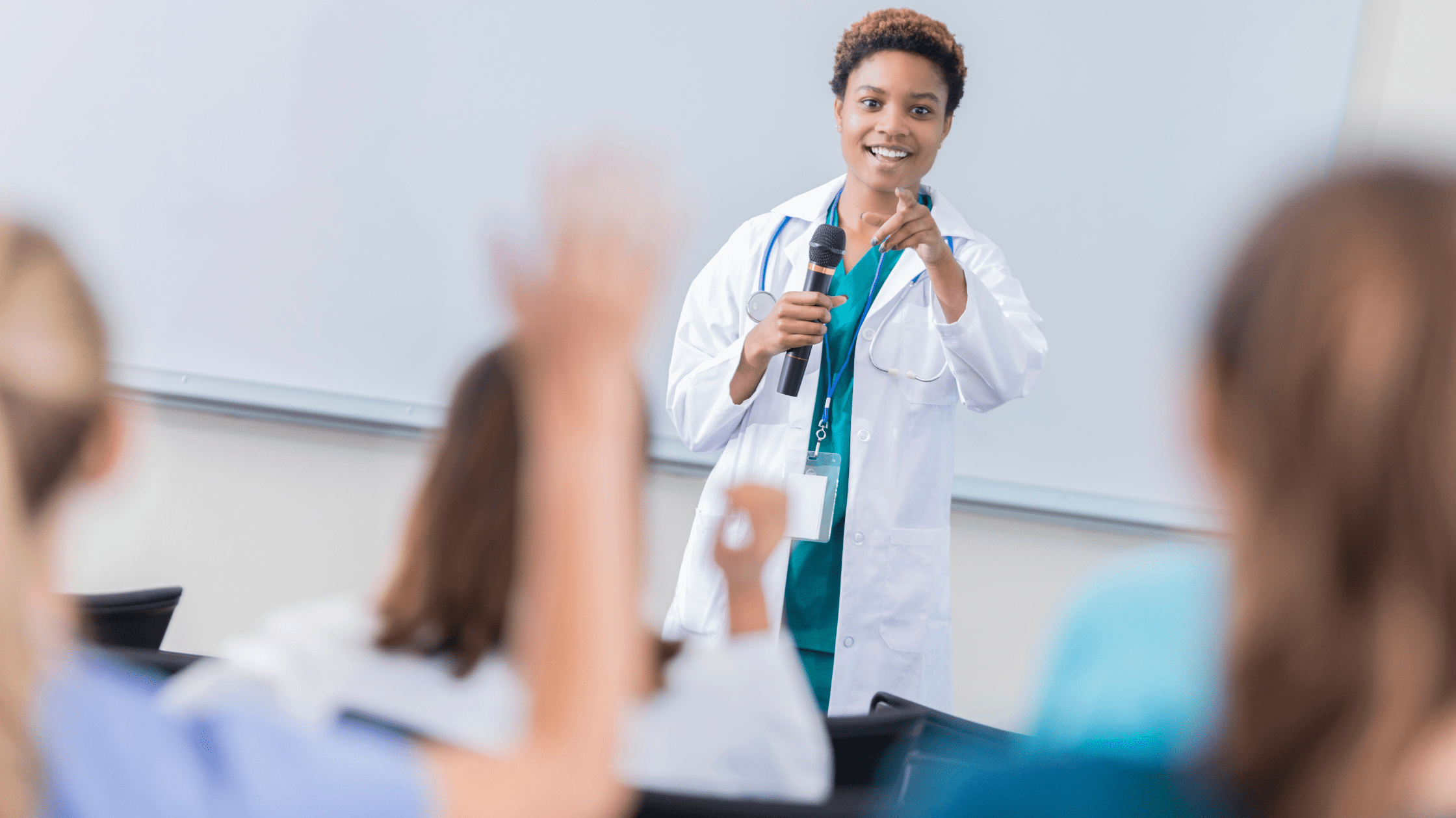 A doctor wearing scrubs answering questions in a medical school classroom.