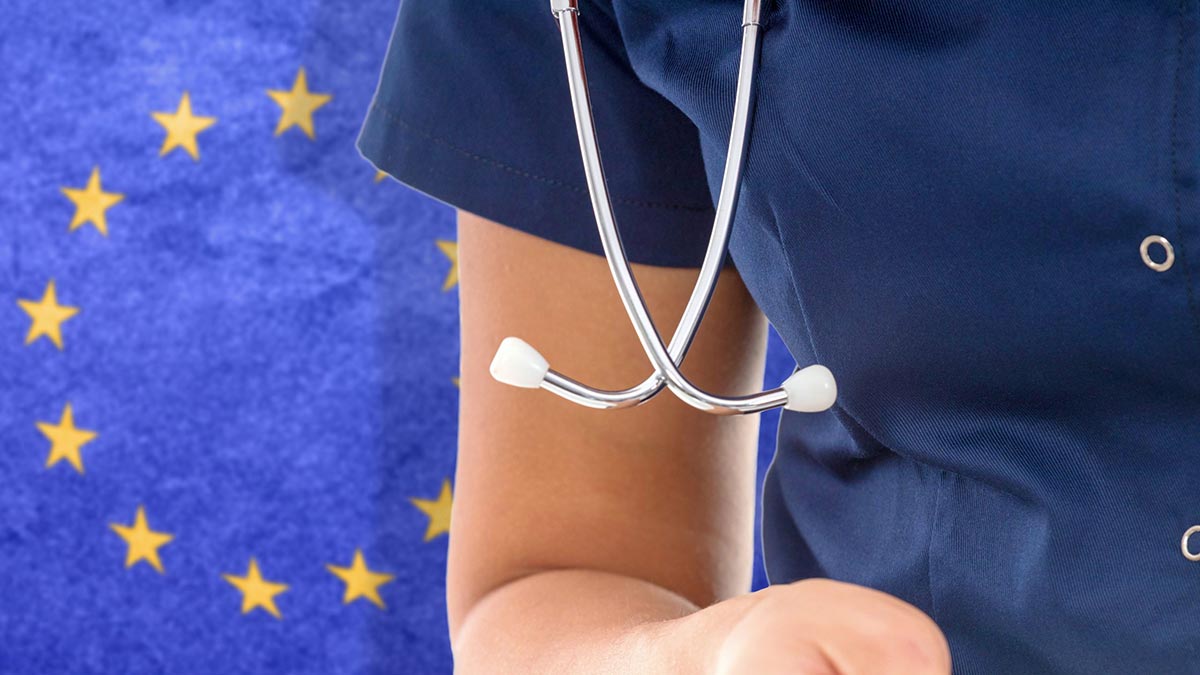 An IMG wearing scrubs standing in front of the European Union flag.