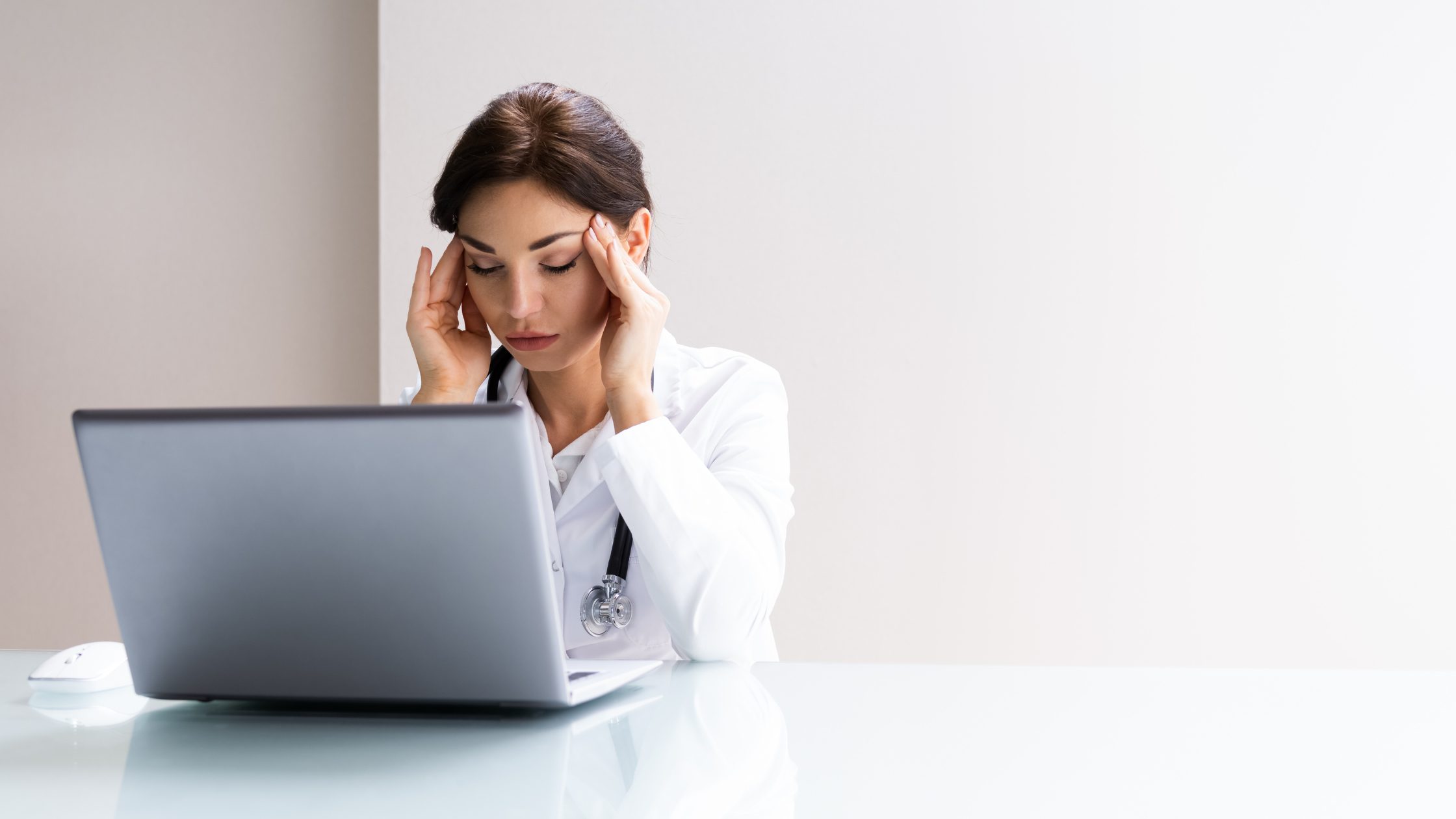 A frustrated resident in a lab coat looking at an open laptop.