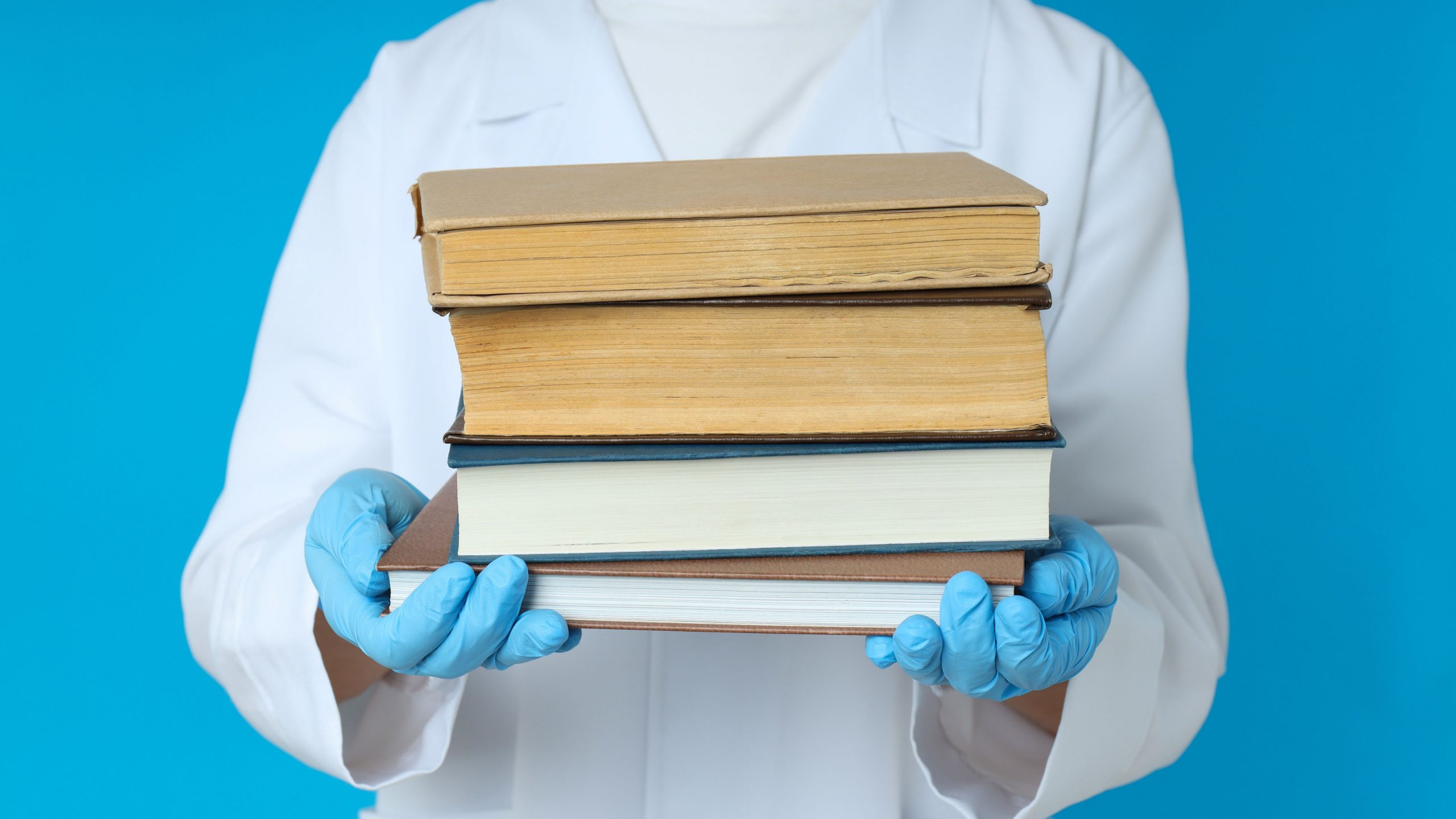 A doctor holding a stack of Step 2CK Biostatistics textbooks.