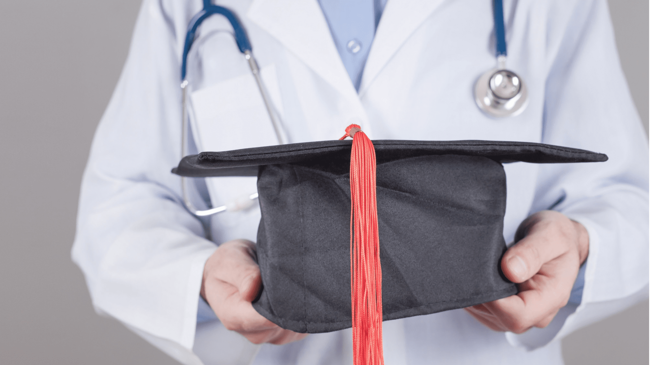 A doctor wearing a lab coat holding a graduation cap after having completed his USMLE Step 3 exam.