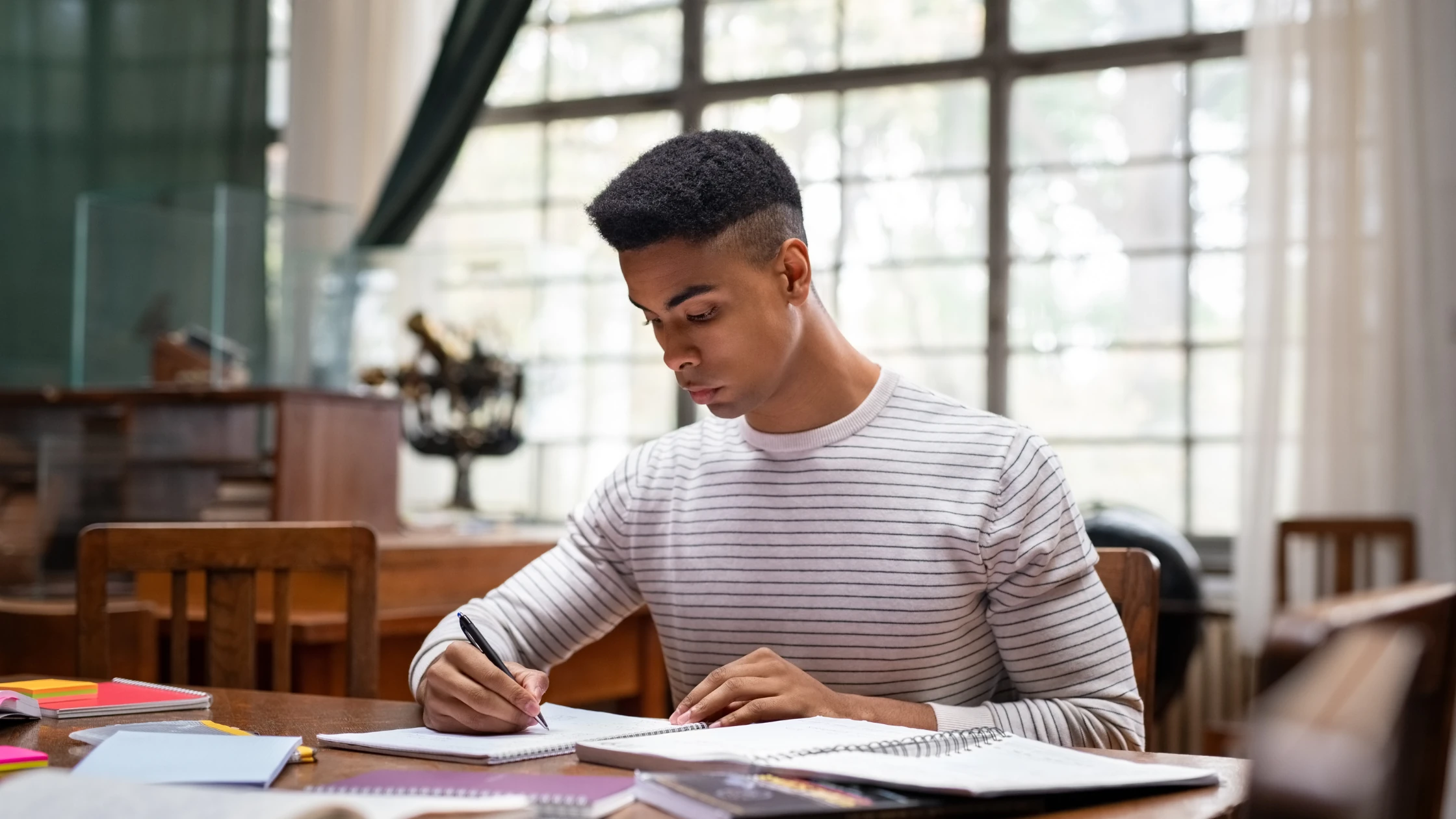 Medical student studying intently at a desk in a well-lit library, surrounded by notebooks and study materials, preparing for the Step 2 CK exam.