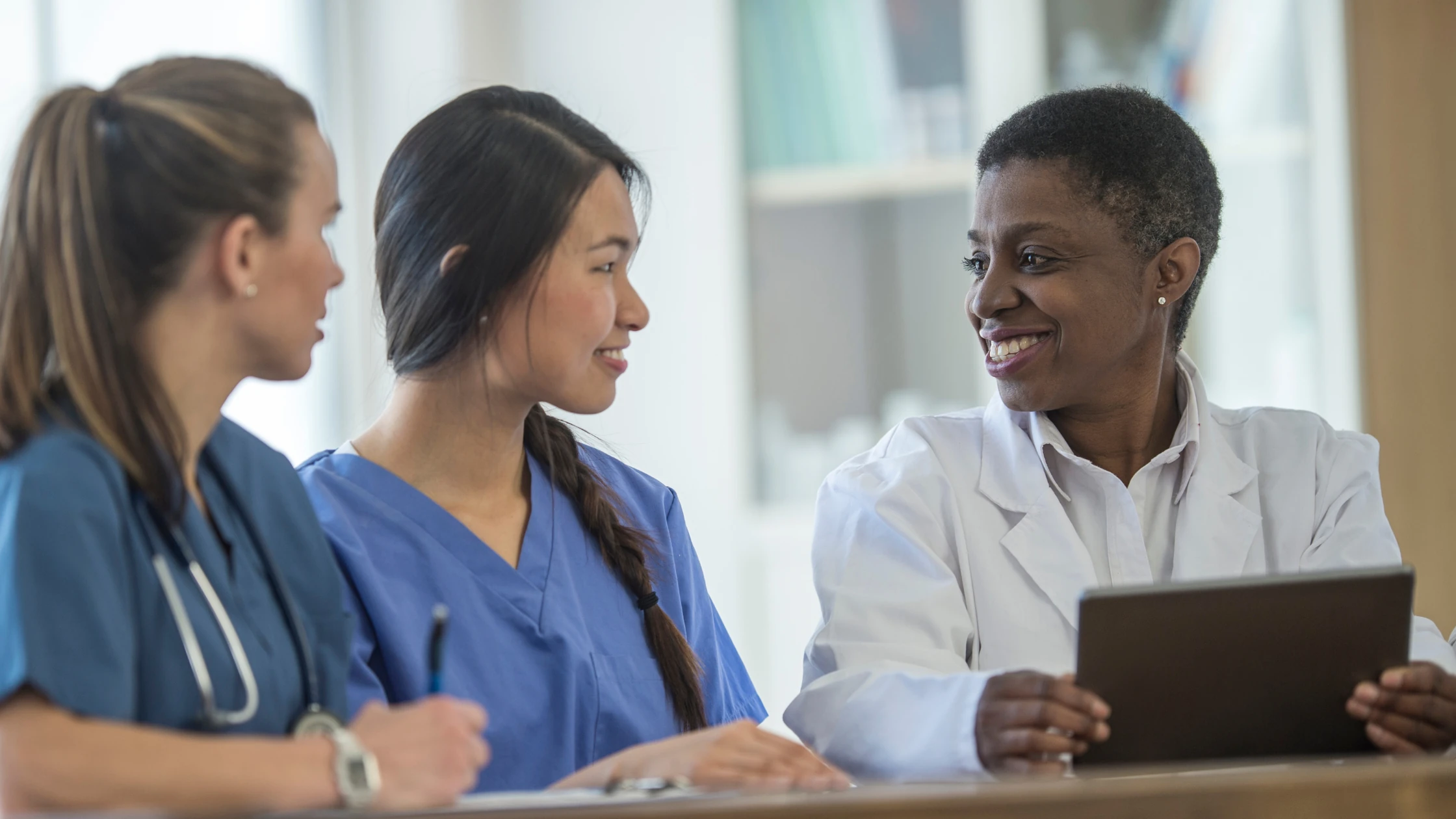 Medical professionals in discussion: a mentor in a white coat providing guidance to two medical students in scrubs.