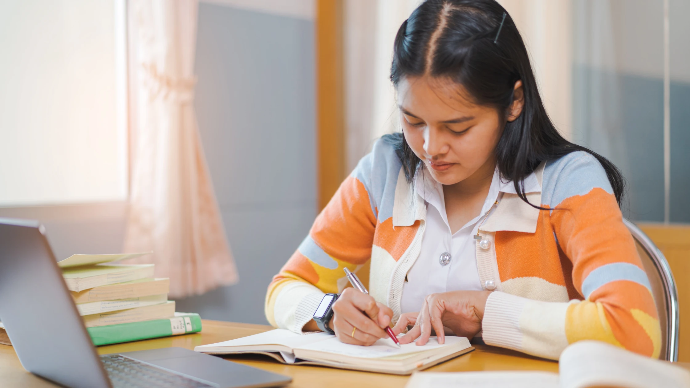 A medical school student studying for the COMLEX level 2 exam, sitting at a desk with a notebook in front of a laptop.