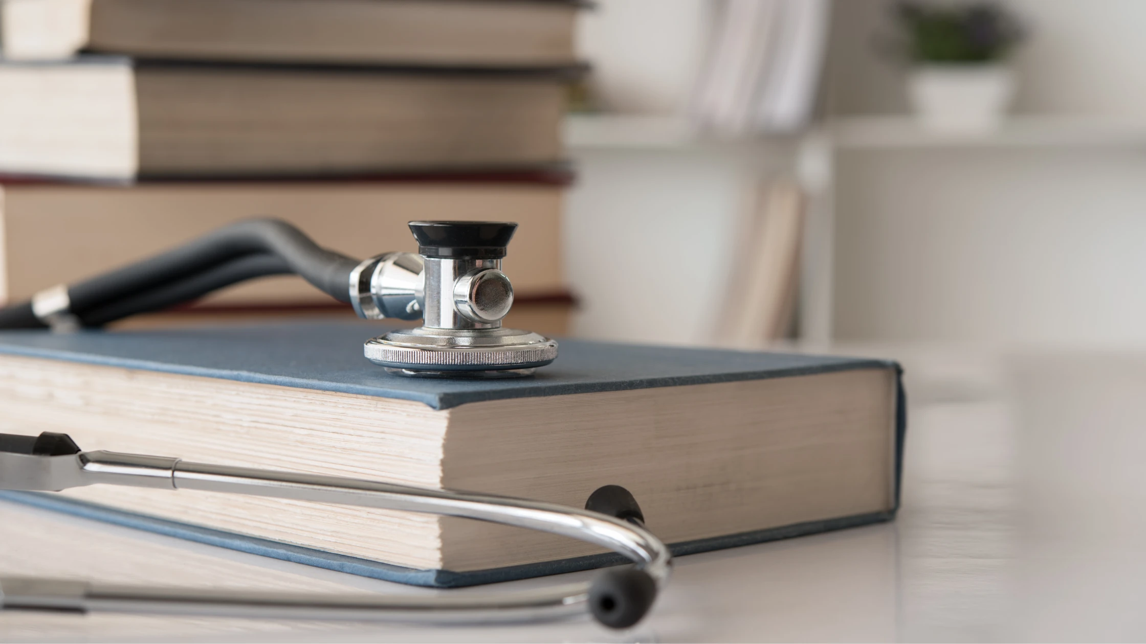 A stethoscope resting on a thick medical book, symbolizing the study and preparation required for medical exams like USMLE and COMLEX.