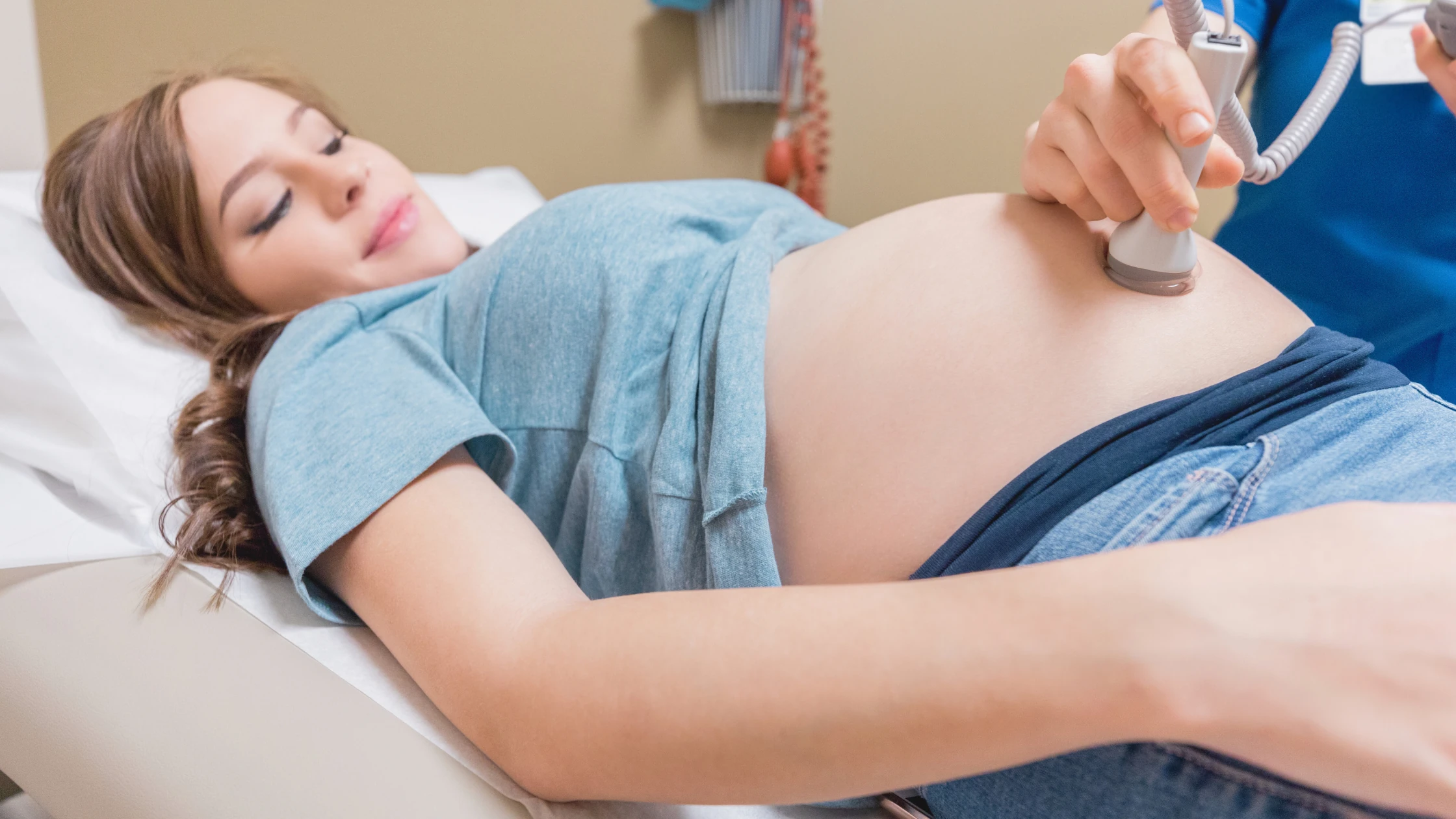 Pregnant woman lying on an exam table while a healthcare provider uses a fetal doppler to listen to the baby's heartbeat.