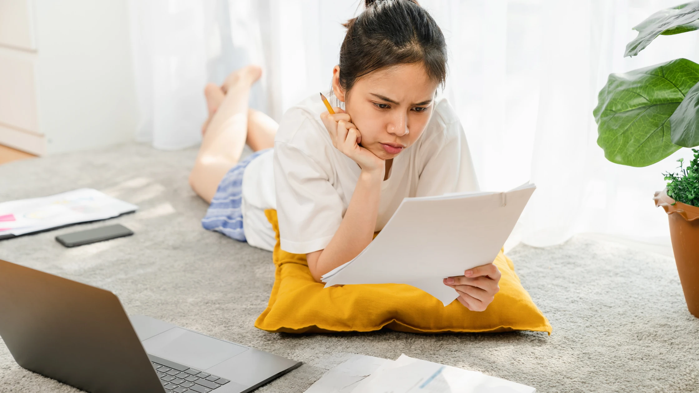 A medical student lying on a rug, studying the USMLE Step 1 Content Outline with a focused expression, surrounded by study materials, a laptop, and natural light from a nearby window.