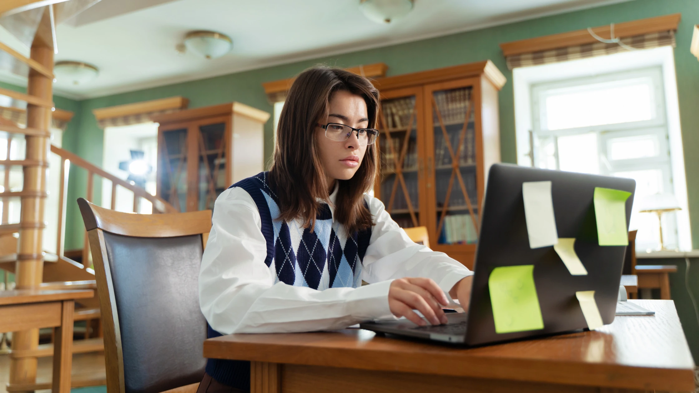 Medical student focused on studying for a USMLE Step 1 retake at a library desk with a laptop covered in sticky notes.