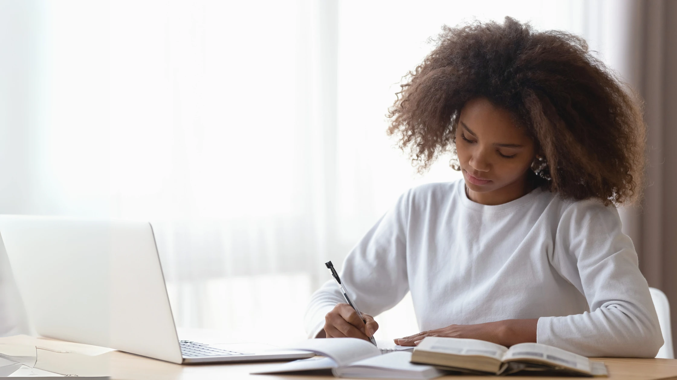 Student focused on studying with a notebook, pen, and laptop, preparing for challenging MCAT questions.