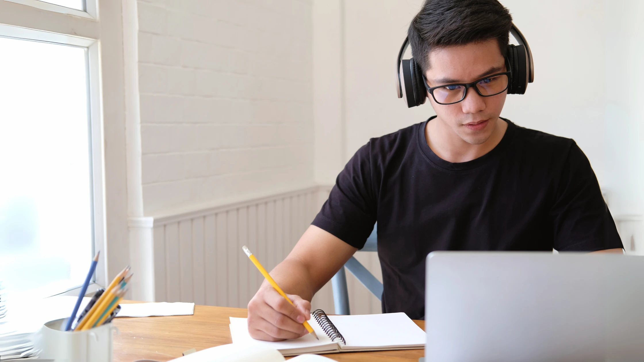 Medical student wearing headphones, studying with a notebook and laptop, creating a study plan for clinical rotations.