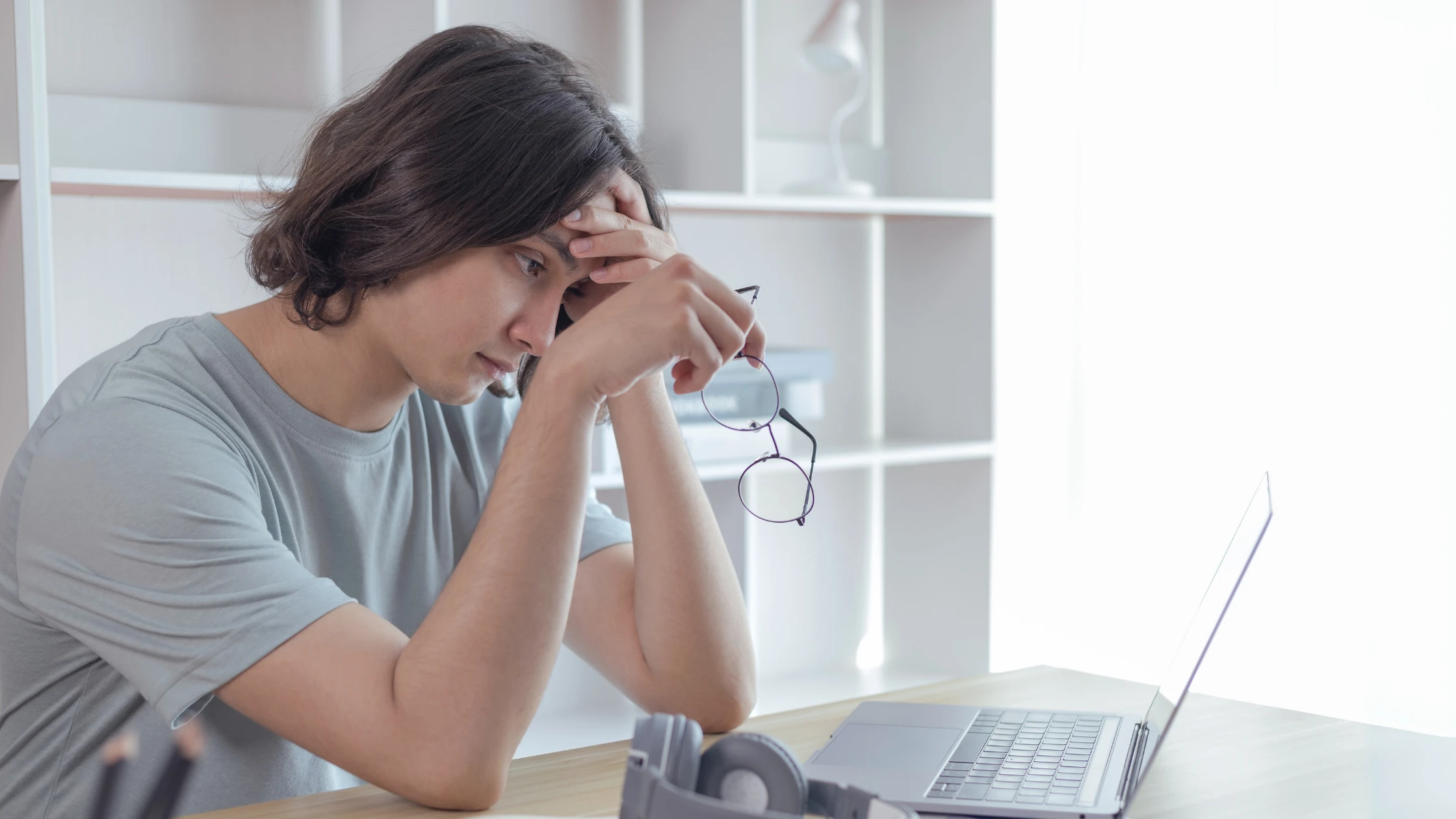 Stressed medical student sitting at a desk, holding glasses and looking at a laptop screen, processing Step 2 CK failure.